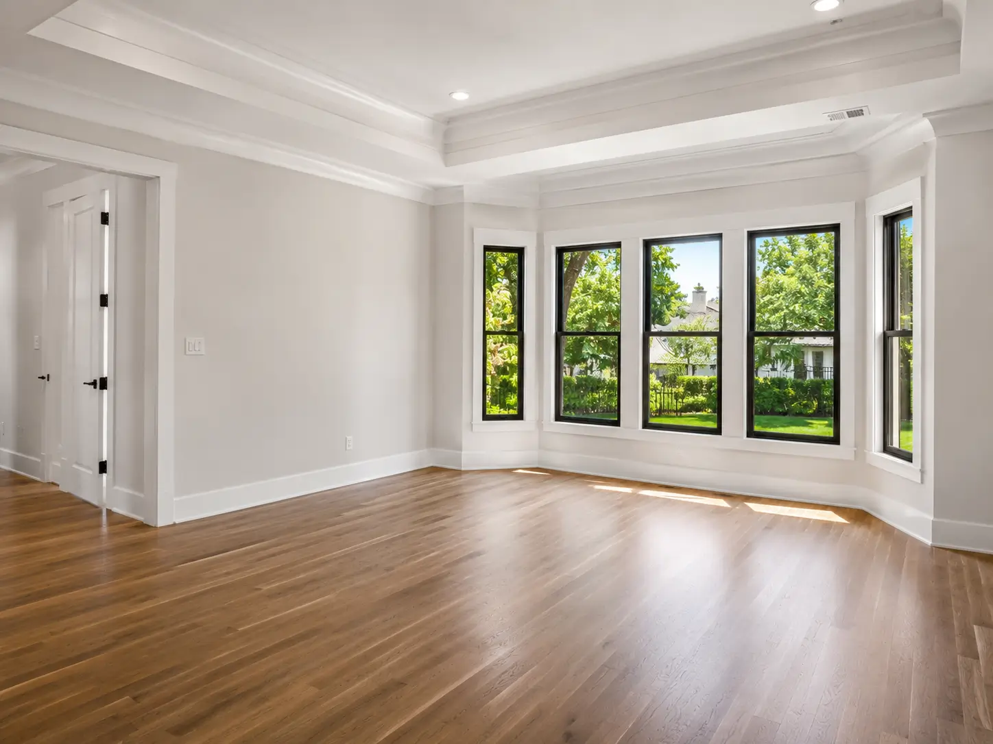 Empty newly painted room with smooth neutral walls, spotless white trim, hardwood flooring, and large windows in a southern residential home